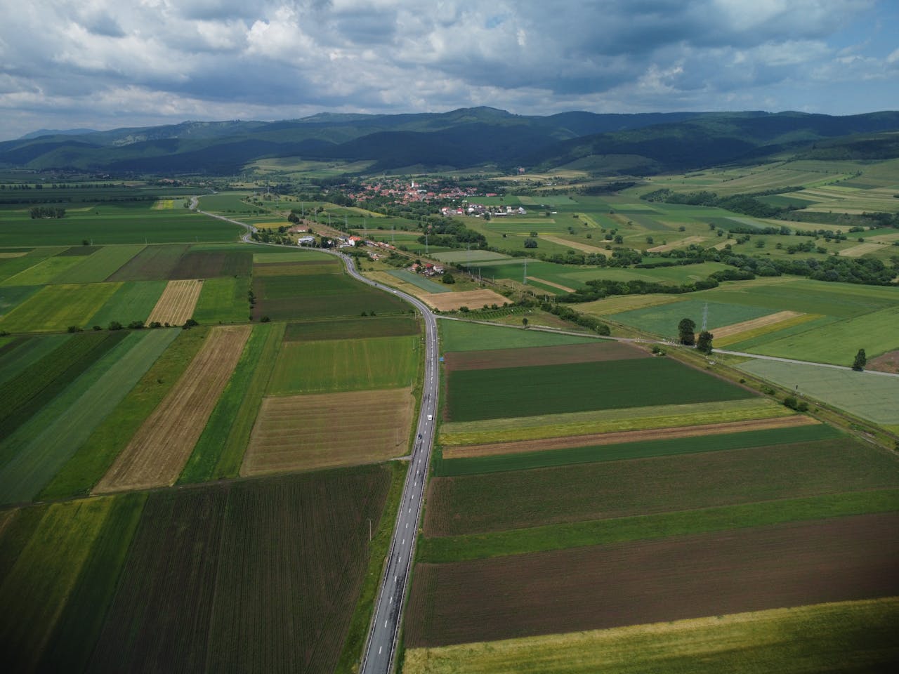 Aerial view of lush agricultural fields surrounding Sfântu Gheorghe under a cloudy sky.