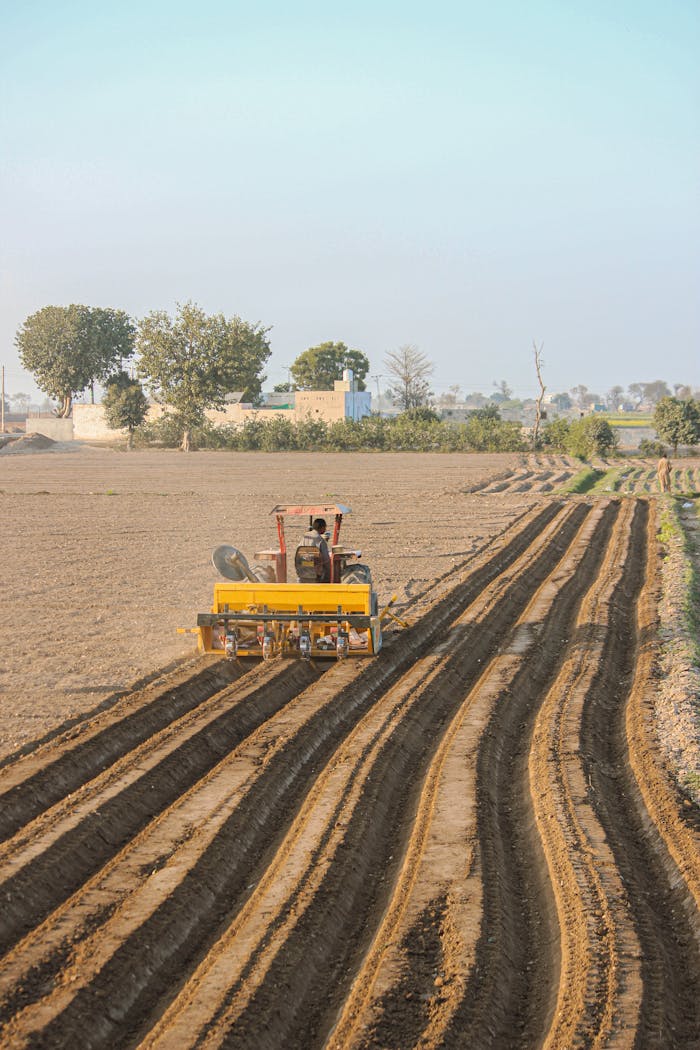 services-bg Aerial view of a tractor plowing fields in Punjab, showcasing rural agriculture and soil preparation.