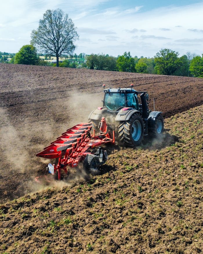 Aerial view of a tractor plowing a field in spring, creating dust clouds as it works the soil.